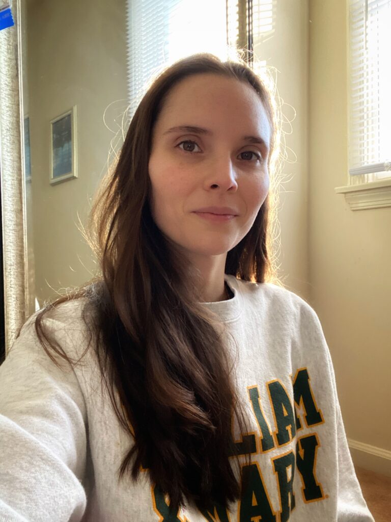 Woman with long, dark brown hair wearing a light grey sweatshirt with the words "WIlliam & Mary" inscribed in emerald green and outlined in yellow