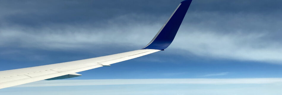 View of the blue sky meeting the blue ocean from an airplane, with the wing of the airplane in the center of the photo